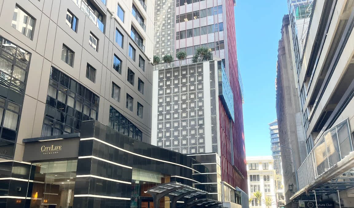 A modern urban building with a glass facade, a prominent 'CityLife Auckland' sign, and a clear blue sky.