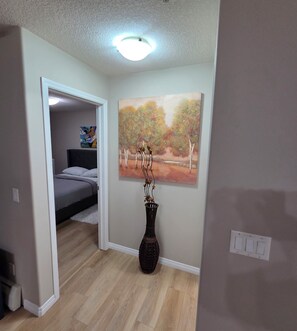A bedroom with a bed, a painting, and a vase on the floor.