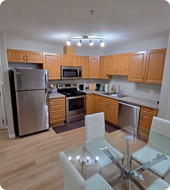 A modern kitchen with wooden cabinets, stainless steel appliances, and a glass dining table.