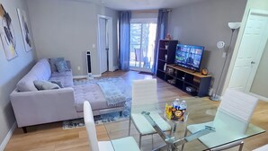 Una sala de estar moderna con una mesa de comedor de vidrio, sillas blancas, un sofá y un televisor.