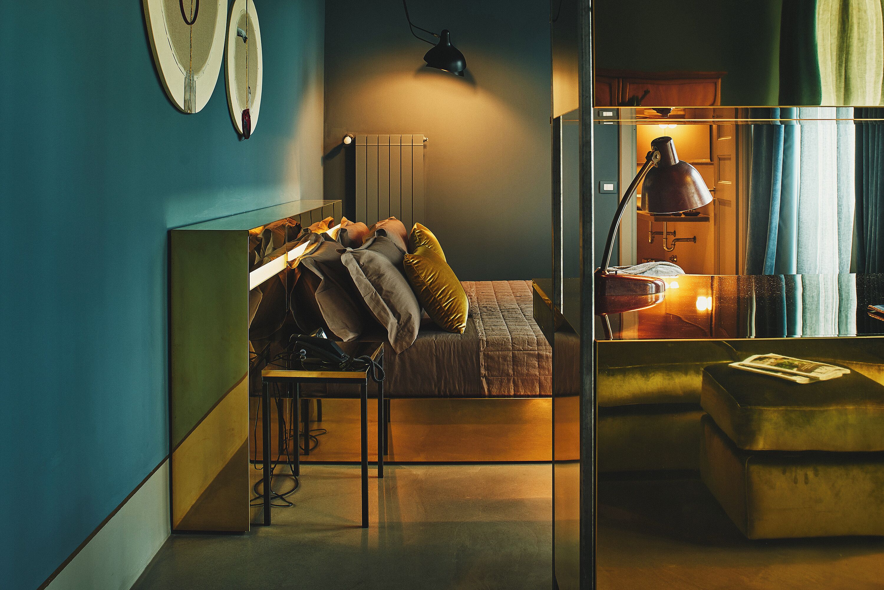 Une chambre à coucher avec un lit, une table de chevet, une lampe et un miroir qui reflète la pièce.
