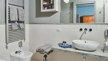 A bathroom with a white sink, a bidet, a towel rack, a mirror, and a medicine cabinet.