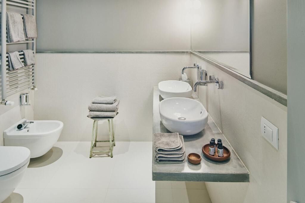 Une salle de bain moderne équipée d’un bidet, de deux lavabos, d’un porte-serviettes et d’un petit tabouret.