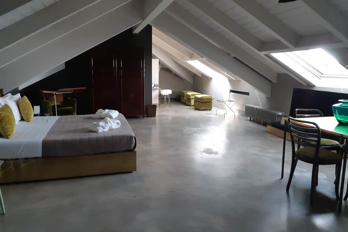 A spacious loft bedroom with a large bed, a dining table, and a high ceiling with skylights.