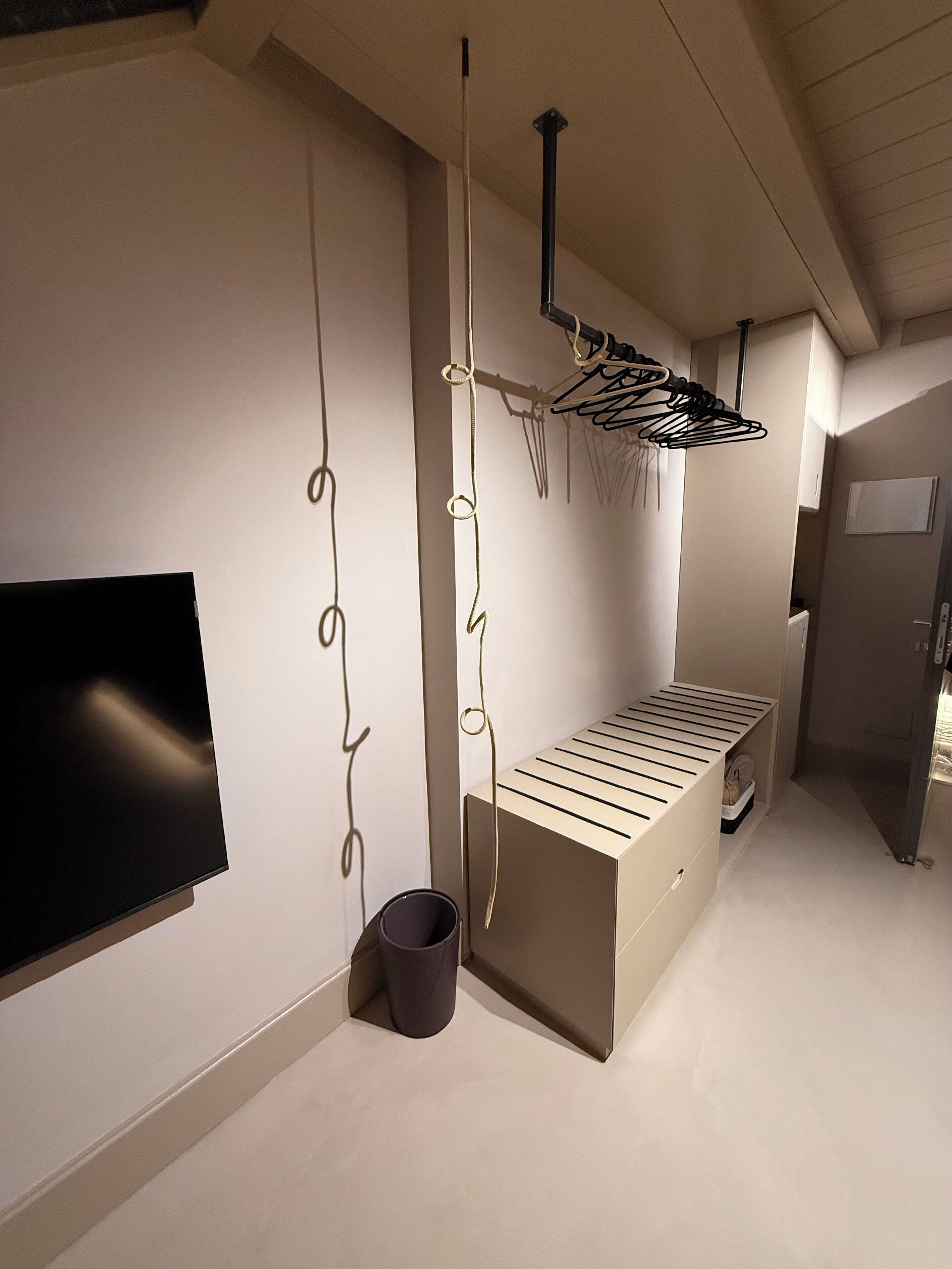 Un intérieur moderne avec un téléviseur à écran plat fixé au mur, un banc doté d’une structure en métal et un portant à vêtements suspendu.