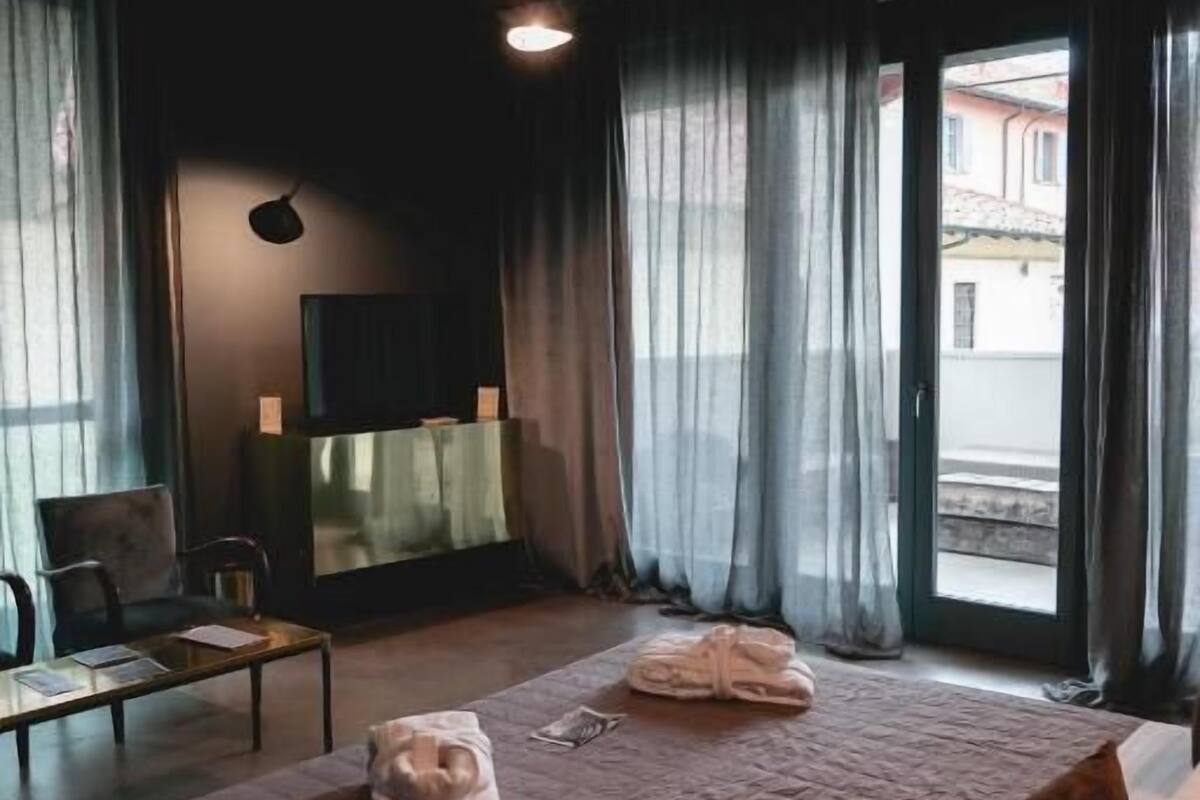 A hotel room with a bed, a desk, a chair, a TV, and a view of the outside.
