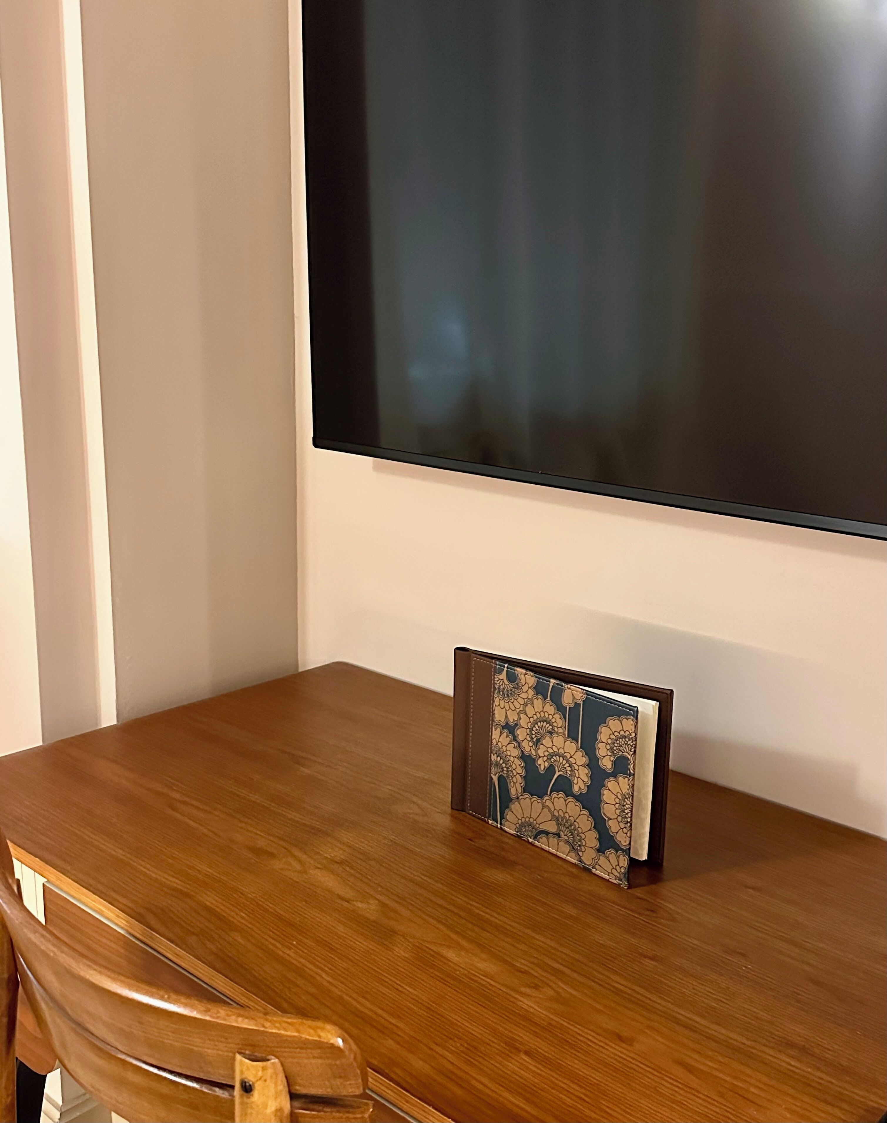 A wooden table with a dark-colored folder on it, positioned in front of a large, dark-colored screen.