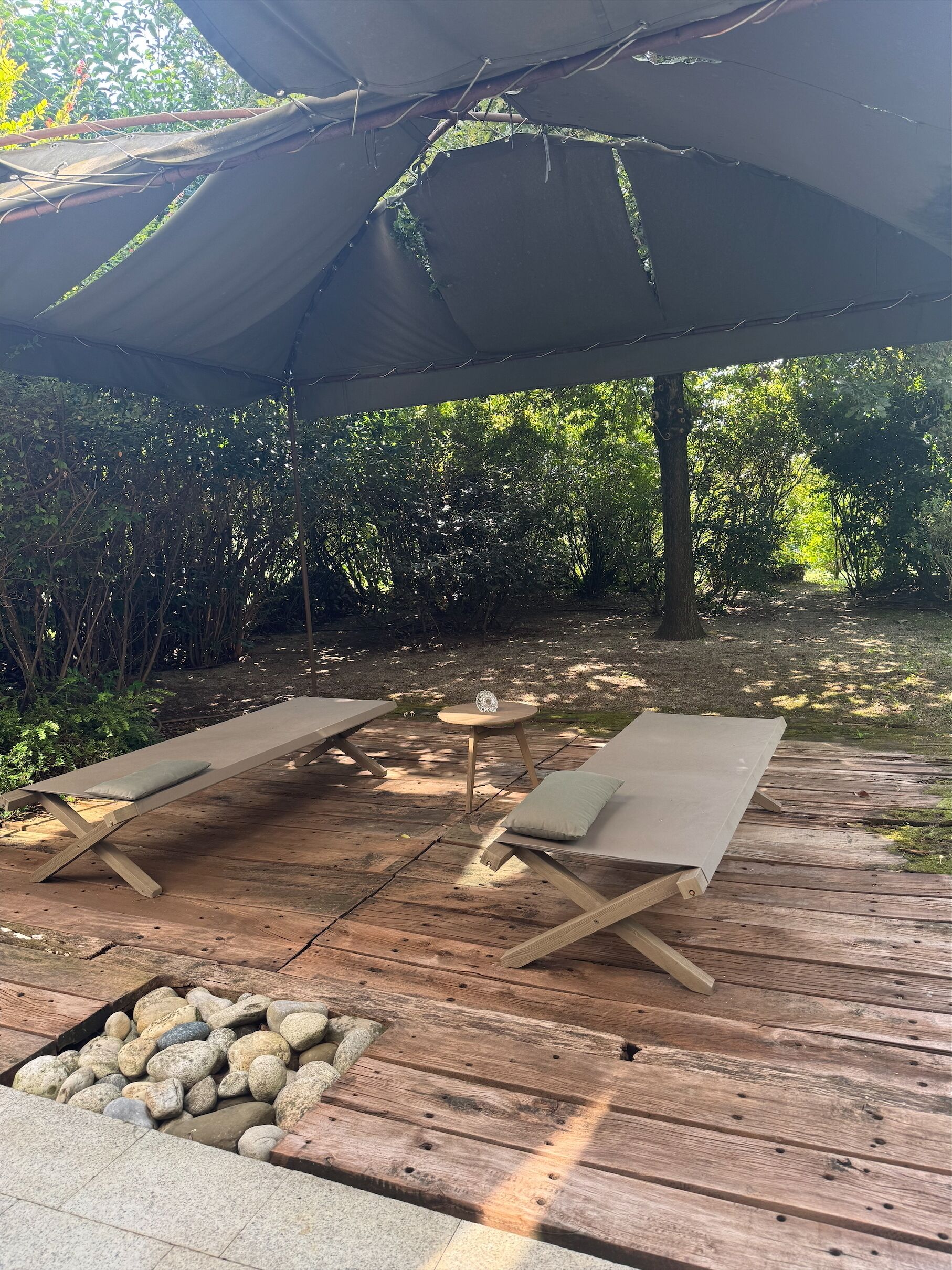 A wooden deck with two lounge chairs and a small table, surrounded by greenery.