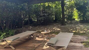 A wooden deck with two lounge chairs and a small table, surrounded by greenery.