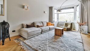 A living room with a sofa, a coffee table, a fireplace, and a large window with curtains.