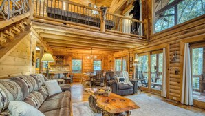 A log cabin interior with a loft bedroom, a dining area, and a large window overlooking the forest. - Rustic Retreat - view-pets-games-hot tub-fire pit (Mineral Bluff)