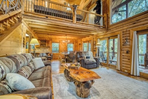 A log cabin interior with a loft bedroom, a dining area, and a large window overlooking the forest. - Rustic Retreat - view-pets-games-hot tub-fire pit (Mineral Bluff)