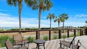 A wooden deck with four chairs and a small table, overlooking a beach with palm trees and a clear blue sky. - 3 Bedroom retreat with private pool (Hilton Head Island)