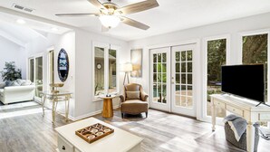 A spacious living room with a ceiling fan, a TV, and a large window offering a view of the outdoors. - 3 Bedroom retreat with private pool (Hilton Head Island)