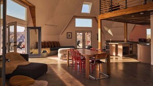 A spacious loft with a high ceiling, a dining area with red chairs, a kitchen with a bar, and a view of the mountains through large windows. - Hawkeye Dome • 112 Acres, Pool & Spa, Epic Views (Yucca Valley)
