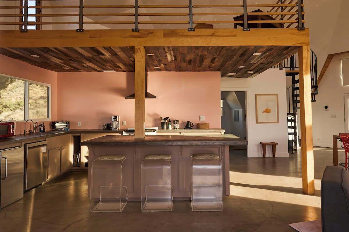 A modern kitchen with a central island, stainless steel appliances, and a wooden ceiling structure.