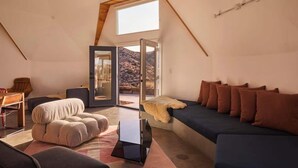 A cozy, modern loft bedroom with a sloped ceiling, a large skylight, a comfortable sofa, a plush ottoman, and a minimalist coffee table. - Hawkeye Dome • 112 Acres, Pool & Spa, Epic Views (Yucca Valley)