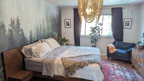 Ein Schlafzimmer mit einem Bett, einem Nachttisch aus Holz, einem Schreibtisch, einem Stuhl und einem großen Fenster.
