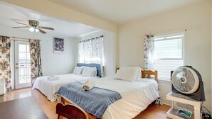 Un dormitorio con dos camas, un ventilador de techo, una ventana con persianas y un ventilador de pie.