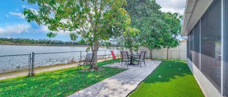 A patio area with a table and chairs, a lawn, and a view of a body of water.