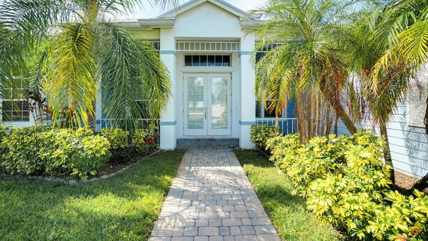 A house with a paved pathway leading to a white door, surrounded by lush greenery and palm trees. - Swim & Golf: Family Home 2 Mi to Clover Park! (Port Saint Lucie)