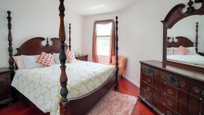 A four-poster bed with a white and yellow patterned bedspread, a wooden dresser with drawers, a nightstand, and a window with curtains. - 5 Mi to Boating! Port St Lucie Home w/ Backyard (Port Saint Lucie)