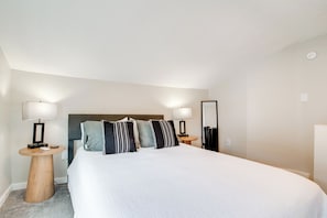 A neatly arranged hotel room with a large bed, two bedside tables with lamps, a mirror, and a carpeted floor. - Hilltopper Convenience: Modern Duplex Near WKU (Bowling Green)