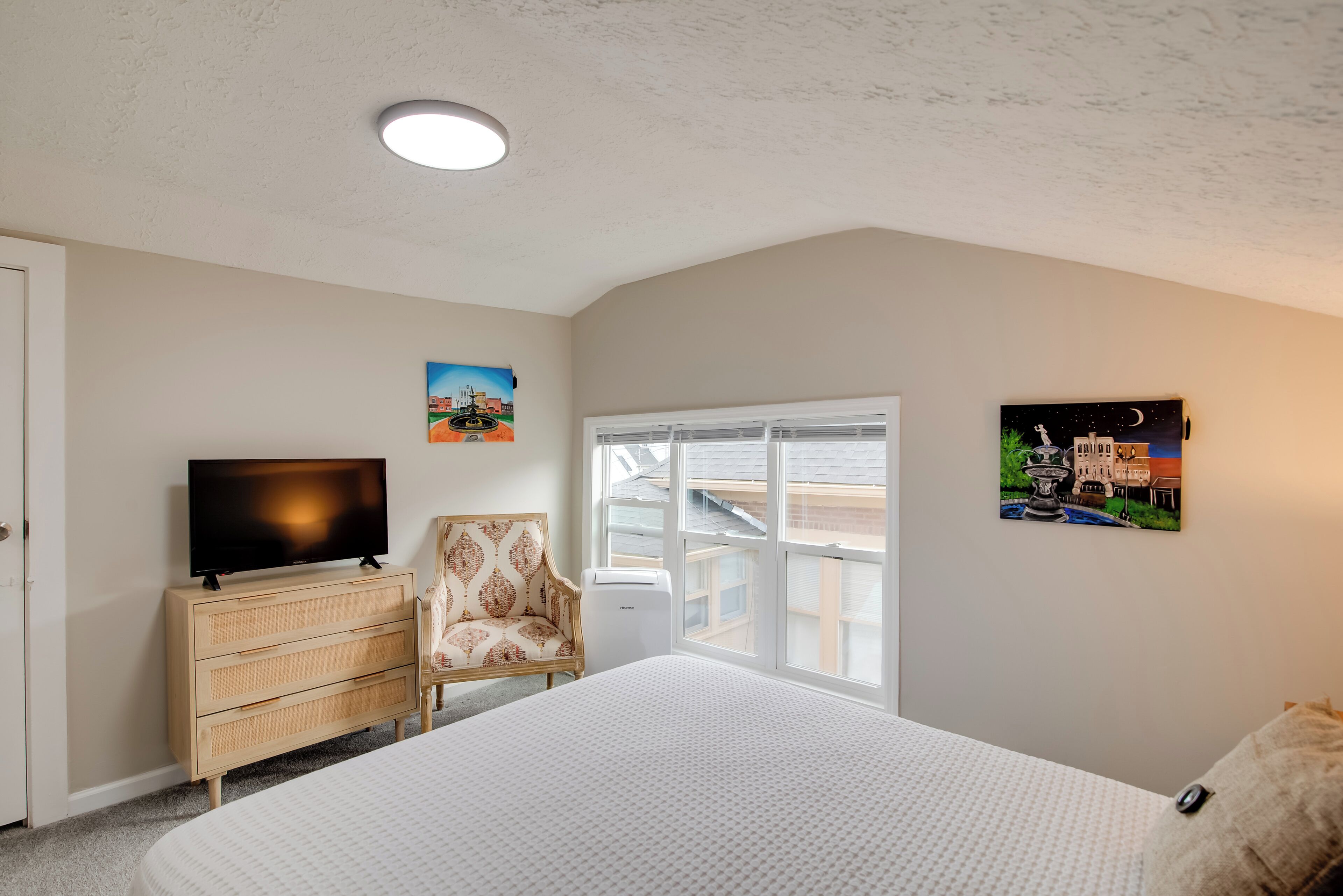 A bedroom with a bed, a dresser, a chair, a television, and two wall-mounted pictures.