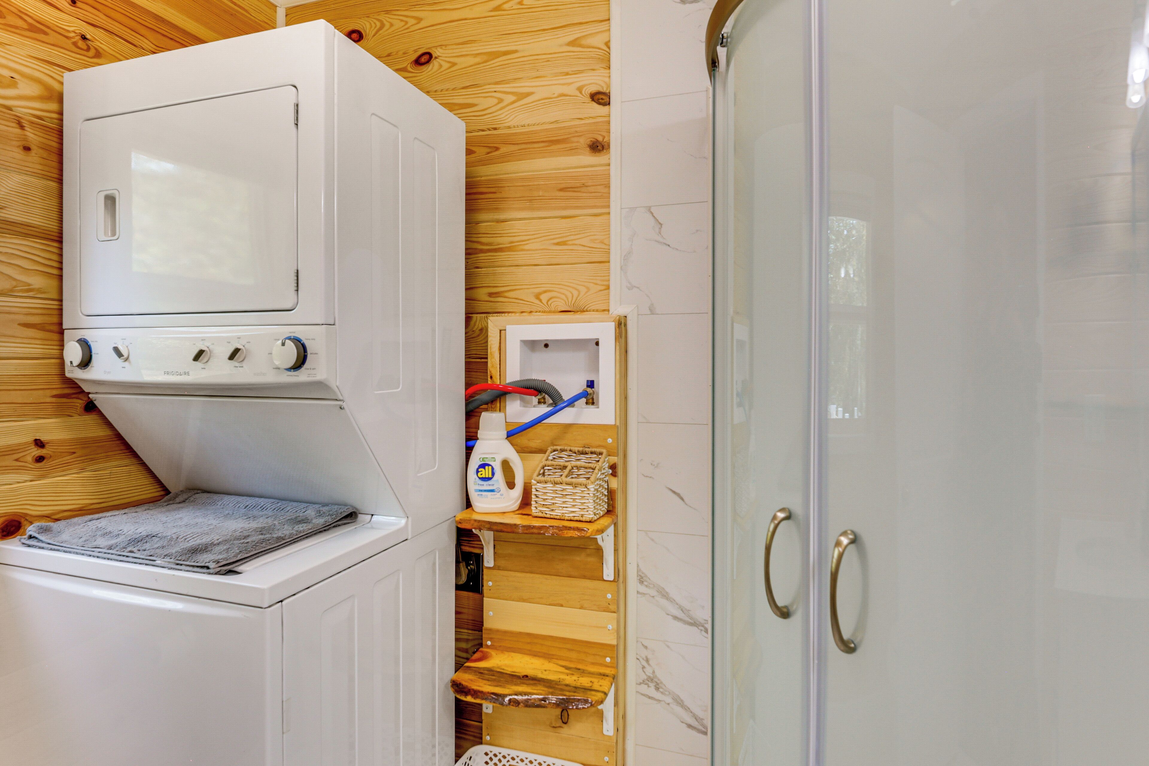 A laundry room with a washing machine, a drying rack, and a small wooden shelf with cleaning supplies.