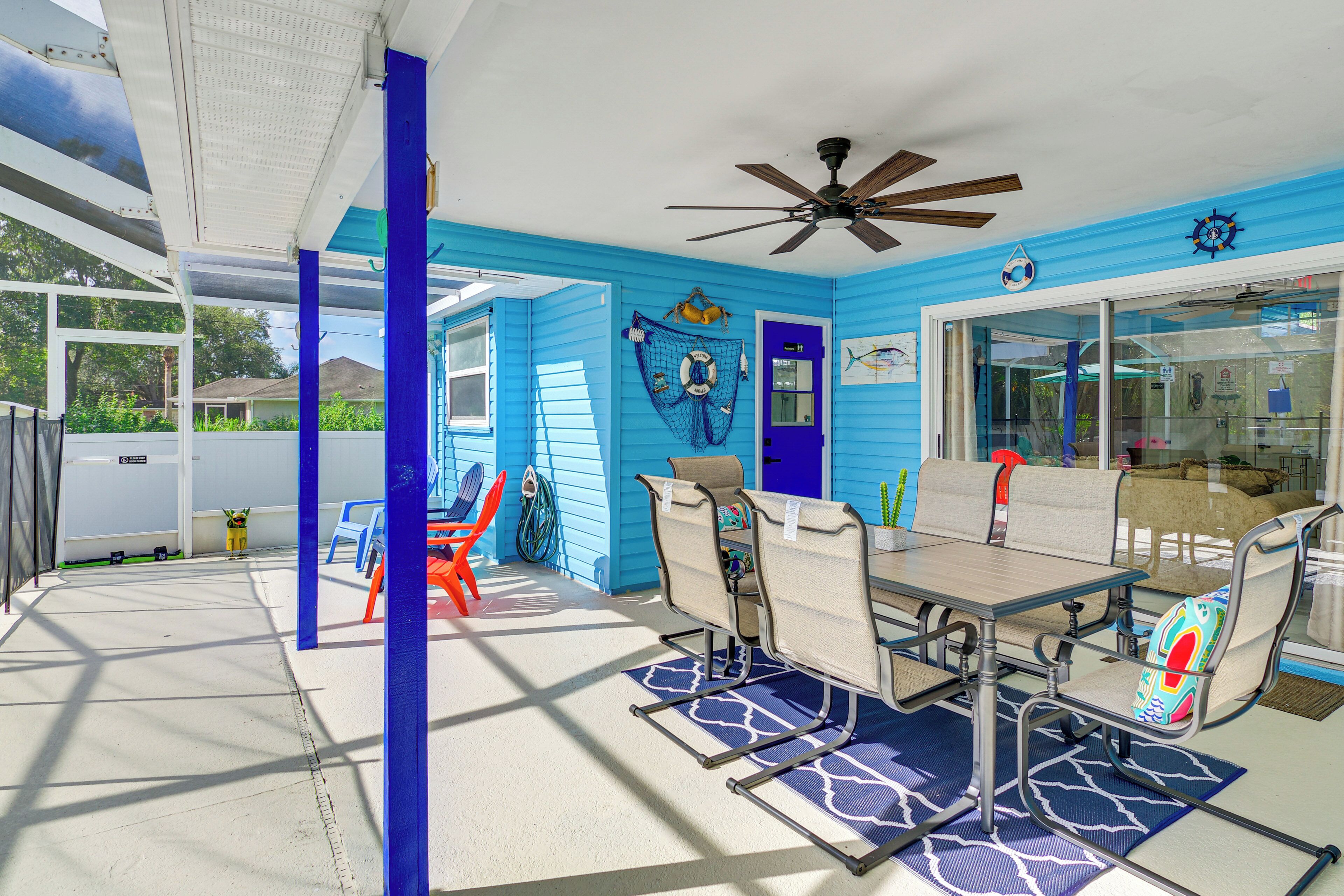 A sunlit patio with a table and chairs, a ceiling fan, and a door with a blue frame.