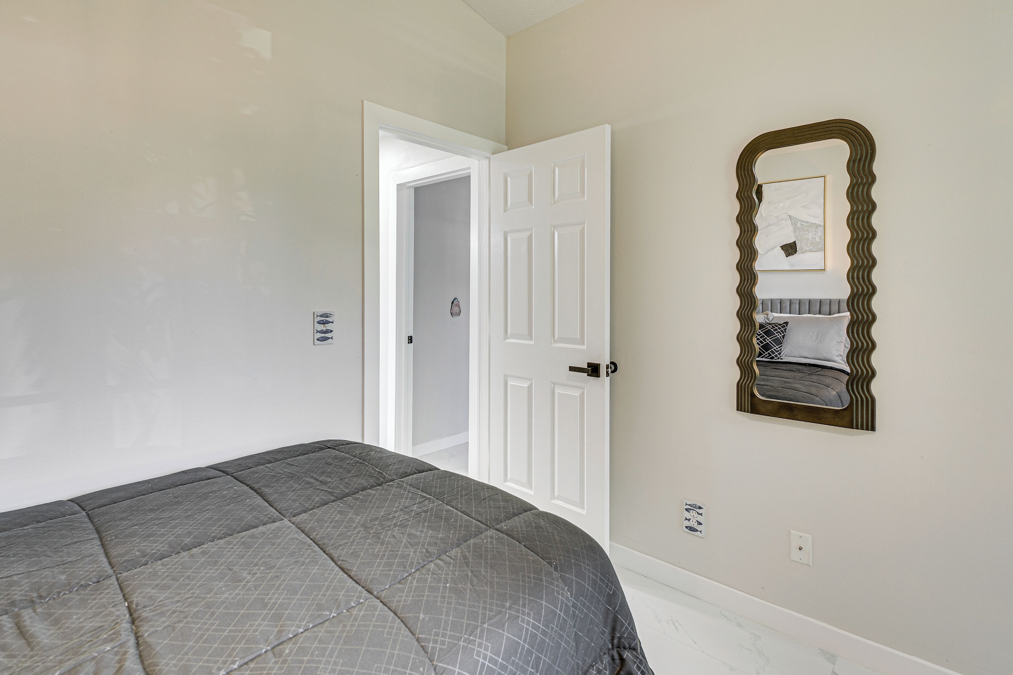 Een slaapkamer met een bed, een deur en een spiegel aan de muur.