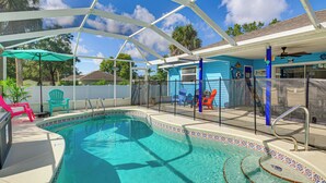 A swimming pool with a covered area, surrounded by colorful chairs and a blue house with decorative elements. - Fenced Yard, Game Room: Family Home in Sebastian! (Sebastian)