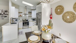 A modern kitchen with white cabinetry, stainless steel appliances, and a dining area with a marble table and gold accents. - Fenced Yard, Game Room: Family Home in Sebastian! (Sebastian)