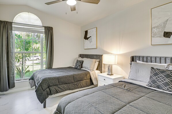 A bedroom with two beds, a ceiling fan, a window with curtains, and a wall-mounted artwork. - Fenced Yard, Game Room: Family Home in Sebastian! (Sebastian)