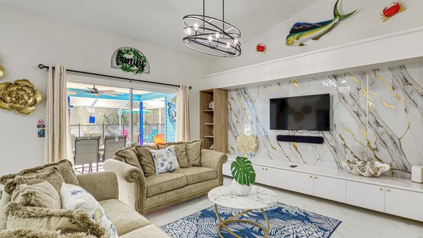 A living room with a beige sofa, a coffee table, a TV mounted on a marble wall, and decorative fish on the wall. - Fenced Yard, Game Room: Family Home in Sebastian! (Sebastian)