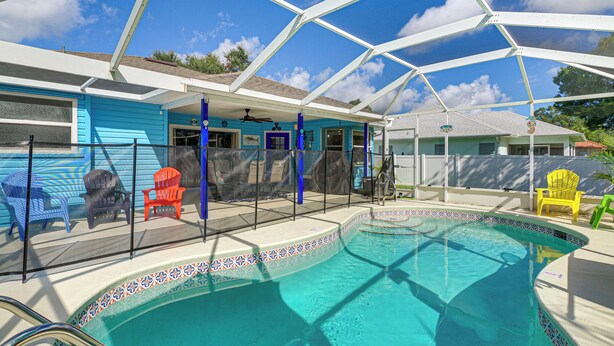 A swimming pool with a covered patio area, chairs, and a fence. - Fenced Yard, Game Room: Family Home in Sebastian! (Sebastian)