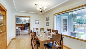 Un comedor con una mesa de madera dispuesta para seis personas, rodeada de sillas, una araña y un ventanal con vistas al exterior.
