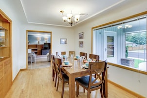 Un comedor con una mesa de madera dispuesta para seis personas, rodeada de sillas, una araña y un ventanal con vistas al exterior.