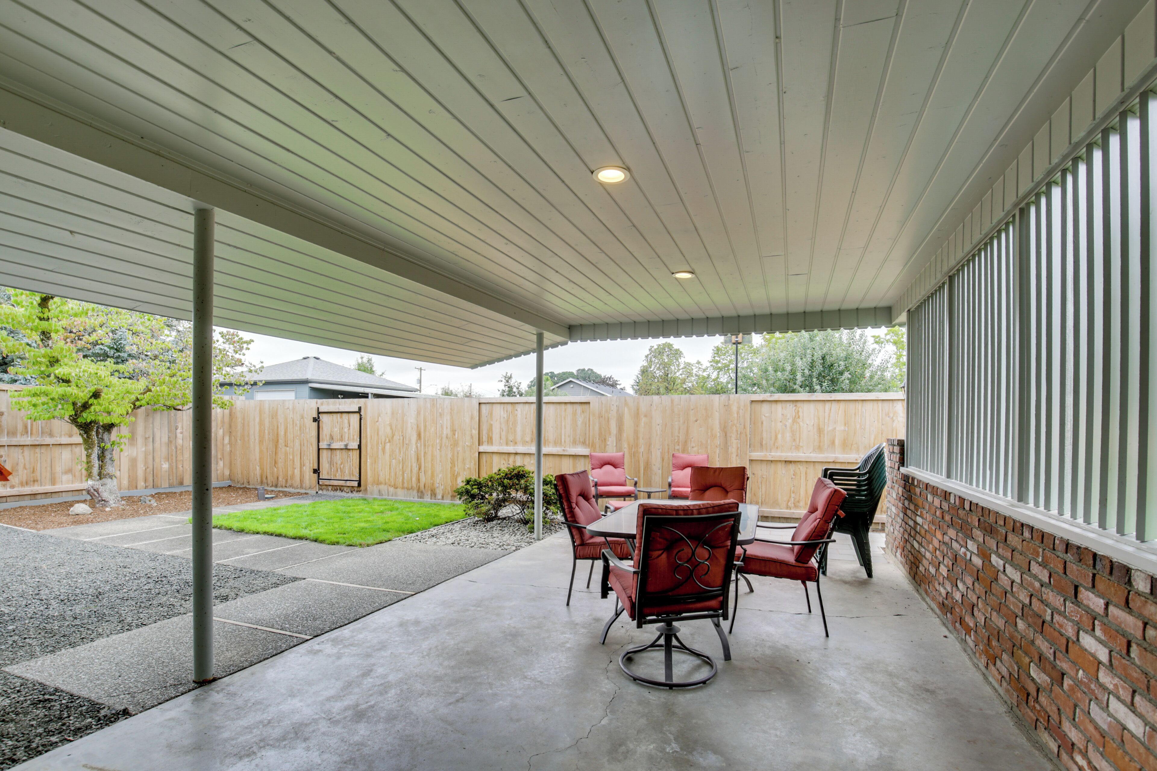 A covered patio area with a concrete floor, a table with chairs, and a brick wall.