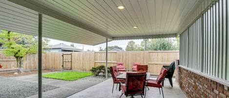 A covered patio area with a concrete floor, a table with chairs, and a brick wall.