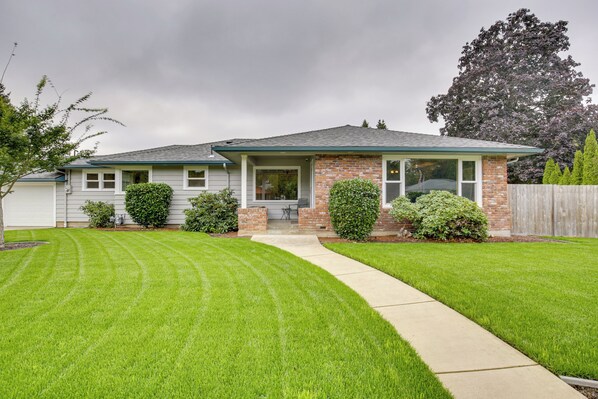 A two-story house with a brick facade, a covered porch, and a well-maintained lawn. - Willamette Valley Family Home w/ Fenced Yard (Albany)