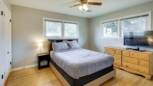 Un dormitorio con una cama, un televisor en una cómoda, un ventilador de techo y dos ventanas.