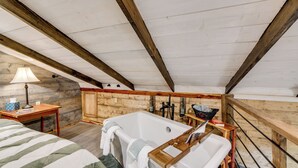 Una camera da letto con un grande letto, un soffitto con travi in legno, una vasca da bagno e una panca in legno.