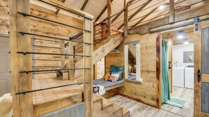 Un interno in legno rustico con un letto a soppalco, una scala e un angolo cottura.