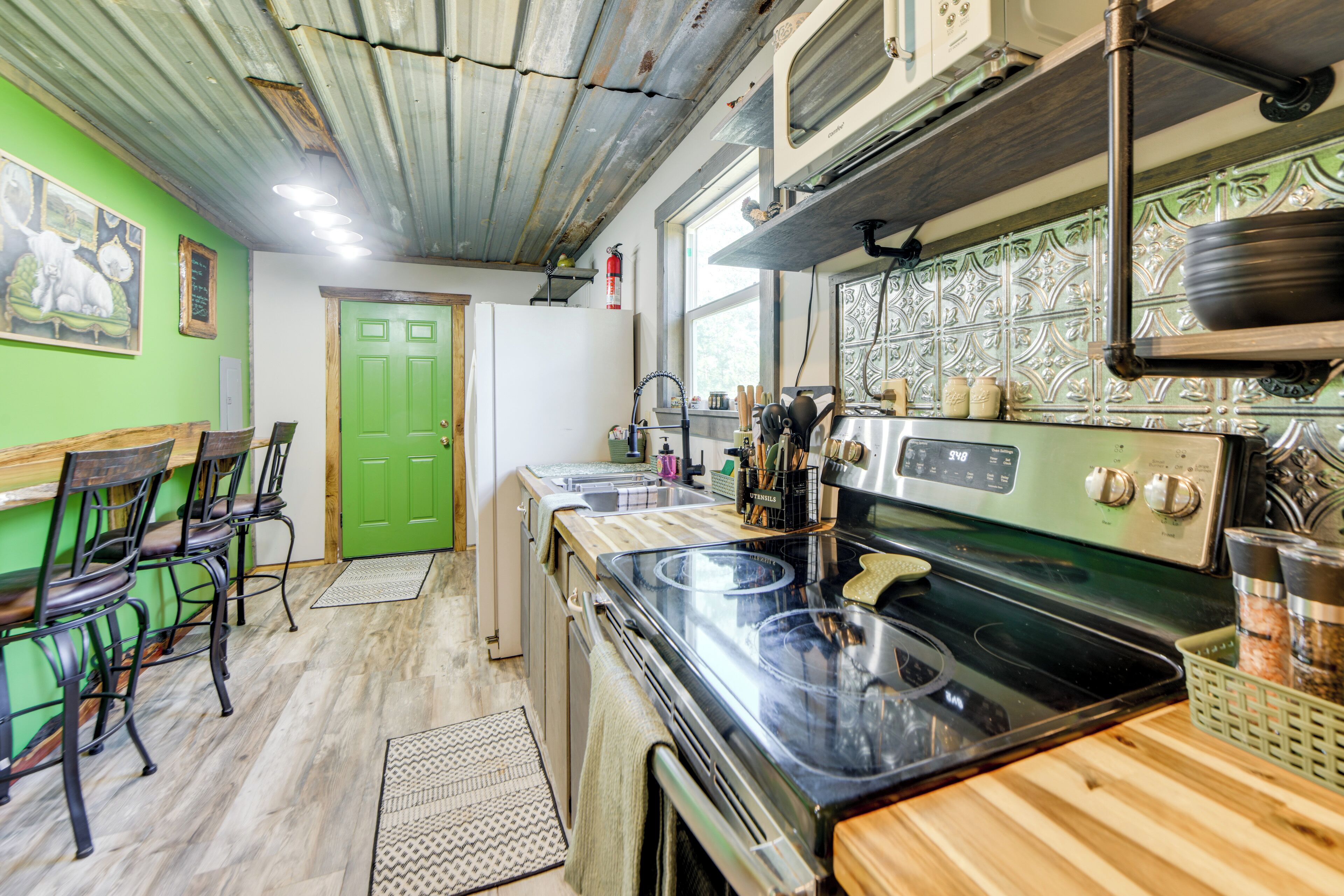 Une cuisine avec une porte verte, des chaises en bois, un poêle et une fenêtre.