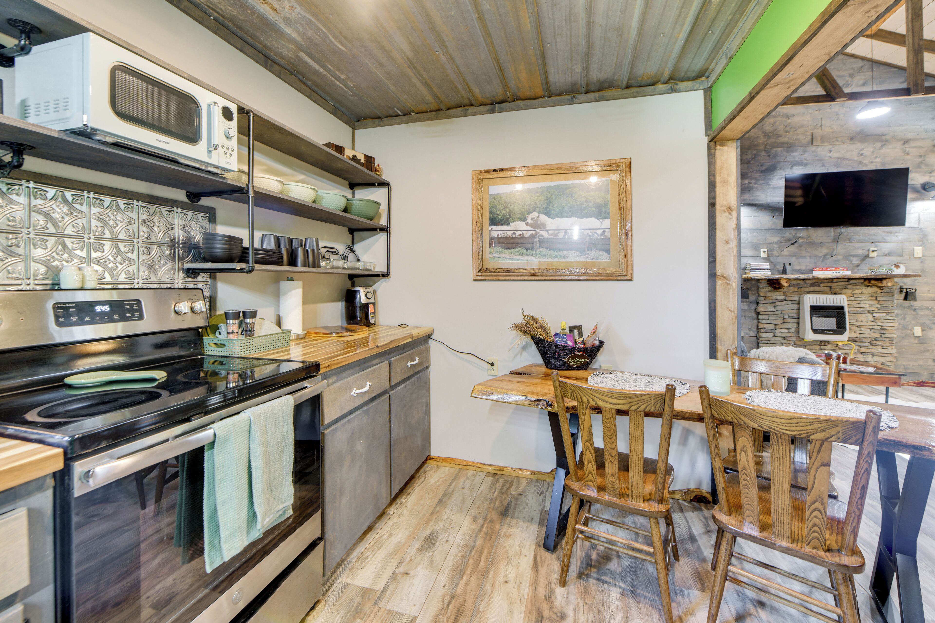 A kitchen with a wooden table and chairs, a microwave, a stove, and a television mounted on the wall.
