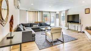 Una sala moderna con un sofá modular, una mesa de centro de vidrio y un televisor montado en un mueble de madera.
