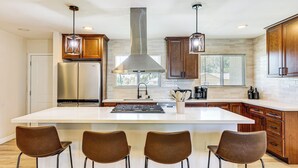 Una cocina moderna con una isla grande, electrodomésticos de acero inoxidable, armarios de madera e iluminación colgante.
