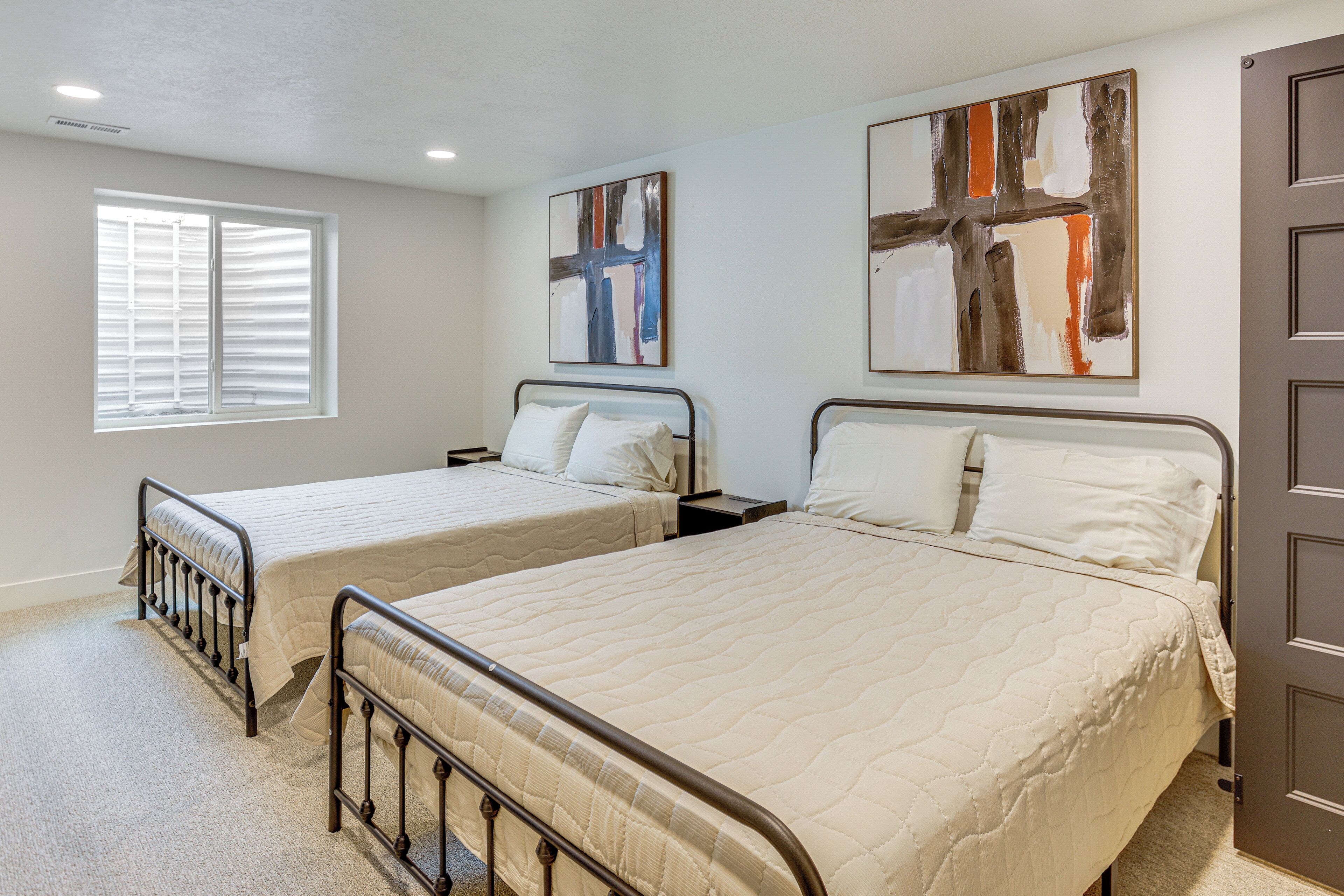 A bedroom with two beds, a window with blinds, and abstract art on the walls.