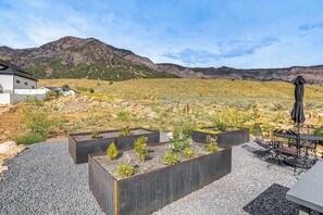 En terrasse med højbede, udendørs møbler og et bjerg i baggrunden.